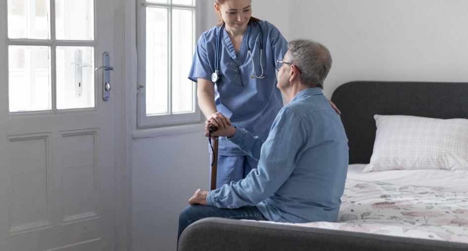 Enfermera junto a anciano que está sentado en una cama