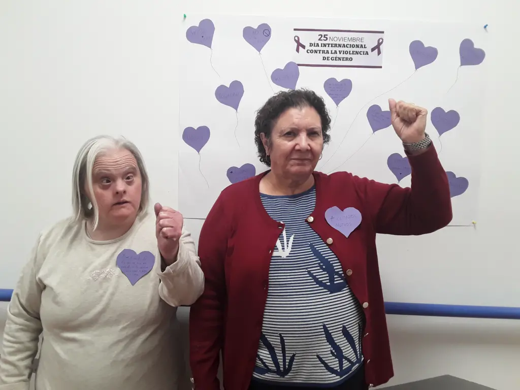 Mujeres de la residencia Escoriza levantando el puño frente a un cartel con corazones morados por el Día Contra la Violencia de Género