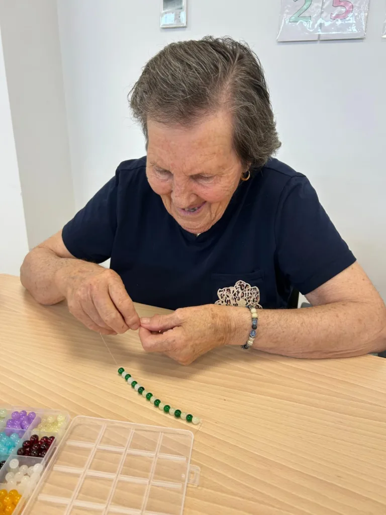 Mujer en la residencia de mayores Alhendín haciendo una pulsera de abalorios en el taller de pulseras
