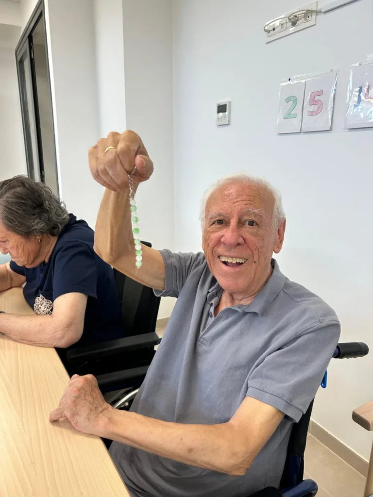 Hombre en la residencia de mayores Alhendín haciendo una pulsera de abalorios en el taller de pulseras